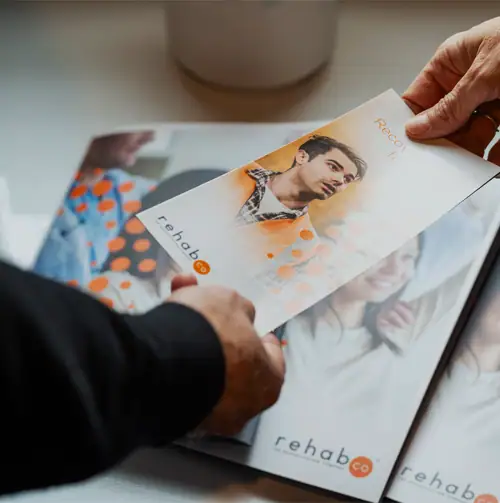 Person holding Rehab Co brochure with health-focused imagery.