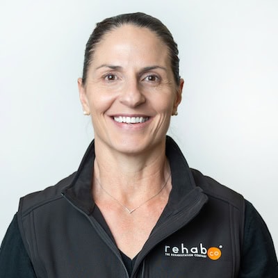 Rehab Co team member smiling, wearing black jacket with logo, in a professional setting.